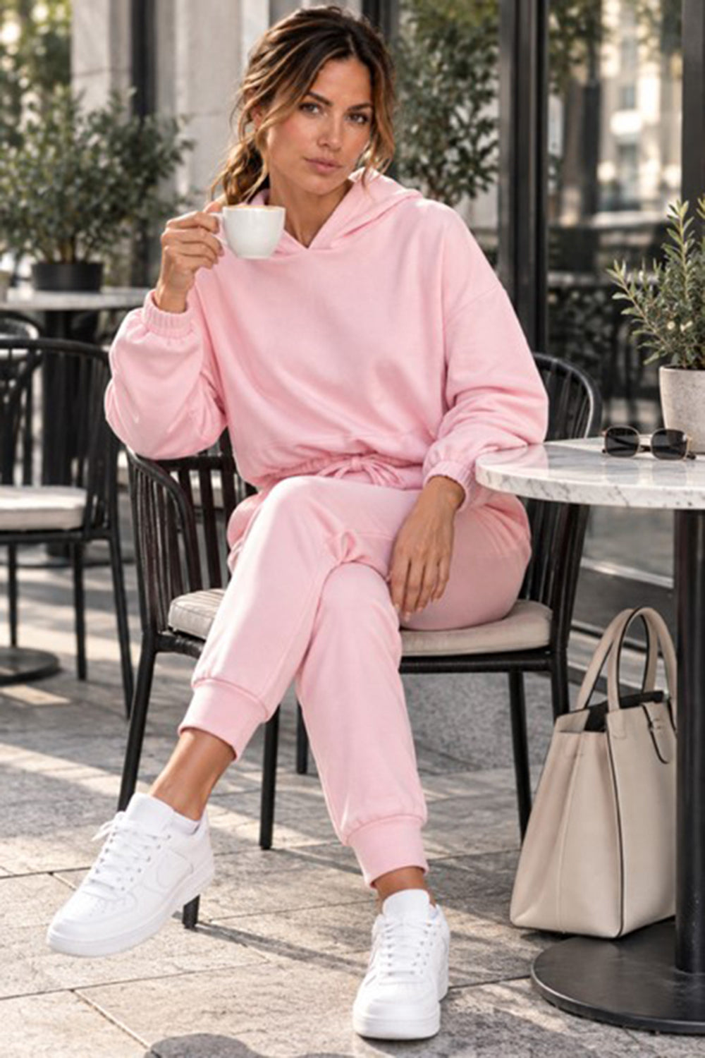 Pink cropped oversized hoodie worn by a model seated at an outdoor café, front view