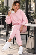 Pink cropped oversized hoodie worn by a model seated at an outdoor café, front view